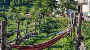A hammock in a lush garden with a view of a hillside and a building in the background.