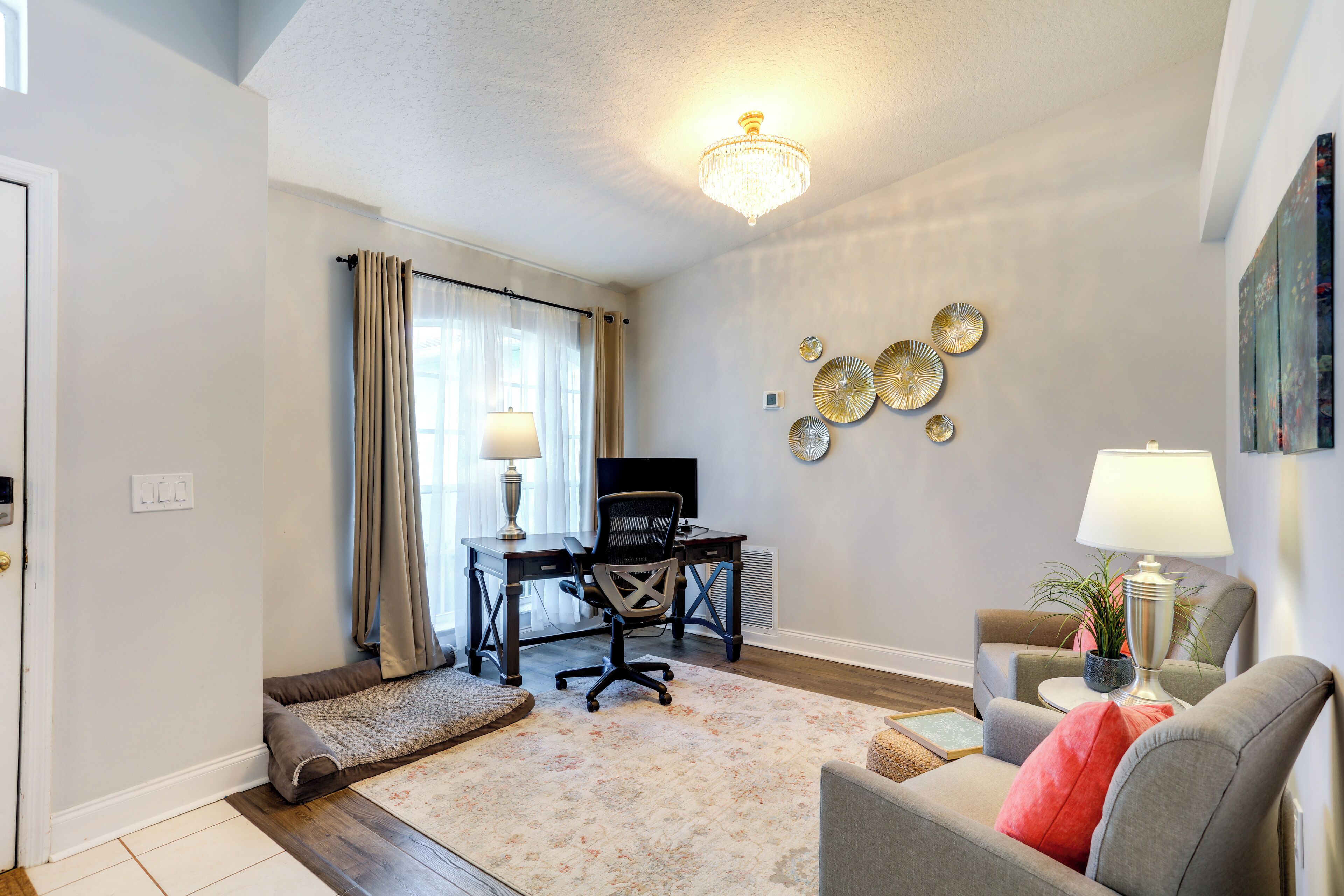 A living room with a desk, a chair, a sofa, a chandelier, and decorative plates on the wall.