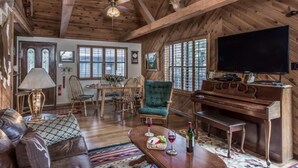 Interior rústico de una cabaña con comedor, sala de estar con piano y televisor.