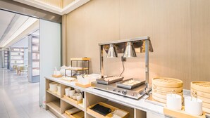 A buffet setup with various food items and utensils, a stove, and a seating area in the background. - Ji Hotel (Shanghai)