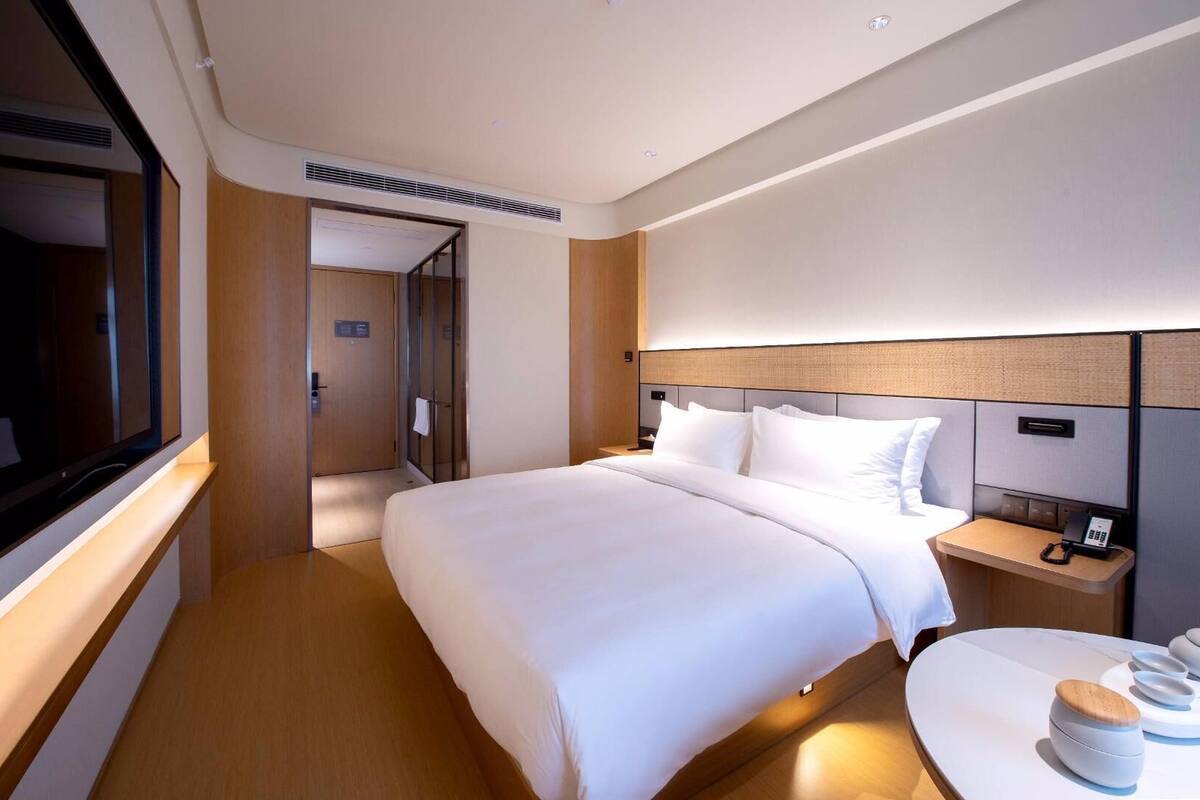 A hotel room with a large bed, bedside tables, a desk, and a television.