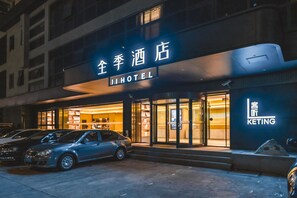 A hotel with a modern facade, illuminated signage, and a car parked in front. - Ji Hotel (Shanghai)