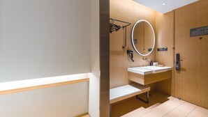 A modern bathroom with a wooden vanity, a large mirror, and a bench. - Ji Hotel (Shanghai)