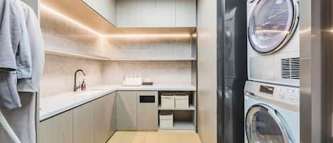 A compact laundry room with a built-in washer and dryer, a sink with soap dispenser, and storage shelves.