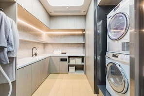 A compact laundry room with a built-in washer and dryer, a sink with soap dispenser, and storage shelves. - Ji Hotel (Shanghai)