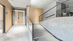 Un intérieur moderne avec un escalier en marbre, des rampes en verre et une porte en bois.