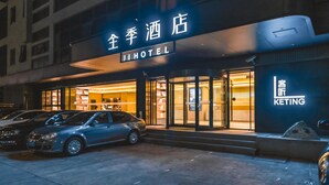 L’entrée d’un hôtel, avec une enseigne en chinois et en anglais, un design moderne et une voiture garée devant.