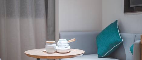 A small round table with two white ceramic containers and a wooden spoon, placed on a light-colored sofa with a teal pillow.