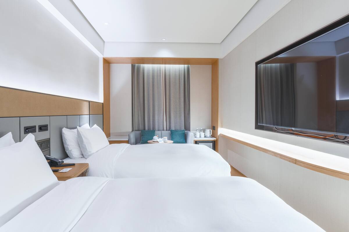 A hotel room with two beds, a TV, a desk, and a window with curtains.
