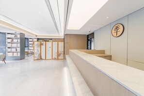 A modern reception area with a marble counter, wooden paneling, and a large wall-mounted sign. - Ji Hotel (Shanghai)