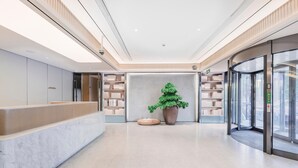 A modern hotel lobby with a reception desk, a large potted plant, and a glass elevator. - Ji Hotel (Shanghai)