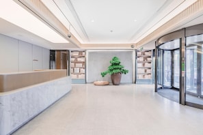 A modern hotel lobby with a reception desk, a large potted plant, and a glass elevator. - Ji Hotel (Shanghai)