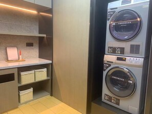 A modern laundry room with a wall-mounted washer and dryer, a shelf with baskets, and a framed picture. - Ji Hotel (Shanghai)