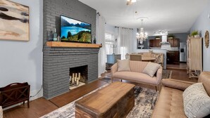 A living room with a fireplace, a television, a sofa, and a dining area in the background.