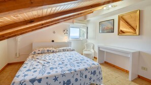 Un dormitorio con techo inclinado, una cama con colcha náutica azul y blanca, un escritorio blanco y una silla.