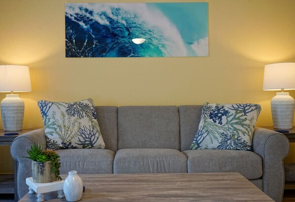A living room with a grey sofa, two patterned pillows, a white vase, and a small plant.