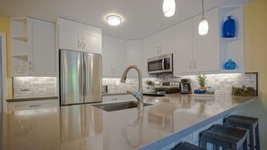 A modern kitchen with stainless steel appliances, a central island with bar stools, and a microwave above the oven. - LOW August   rates  A/C-Free Parking-No Resort Fees (Kihei)