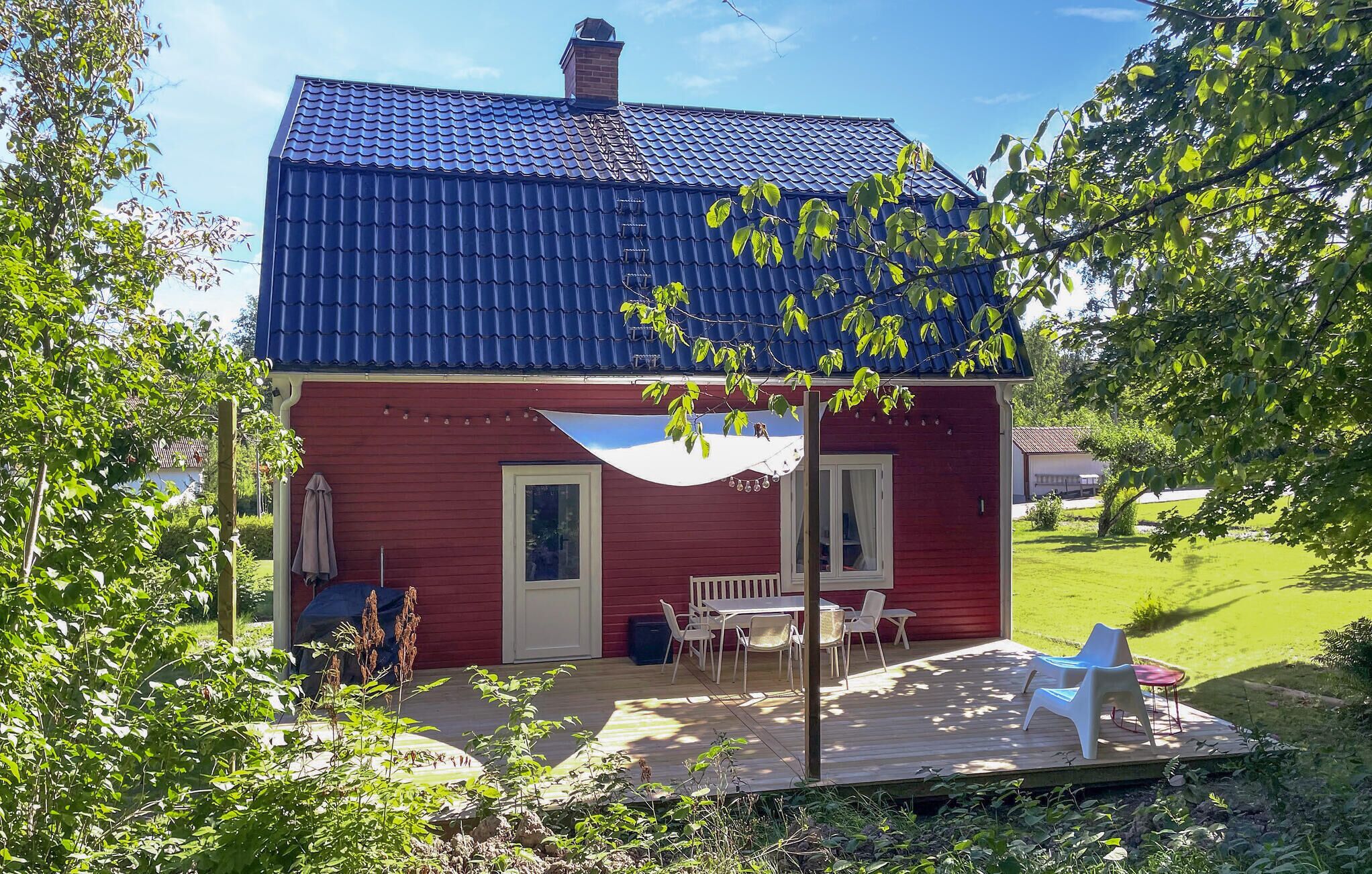 Een rode woning met een blauw dak, een overdekte patio met een tafel en stoelen, en een tuin.