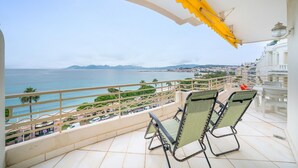 Un balcón con dos sillas verdes, un toldo amarillo y vistas al mar y al paisaje urbano.
