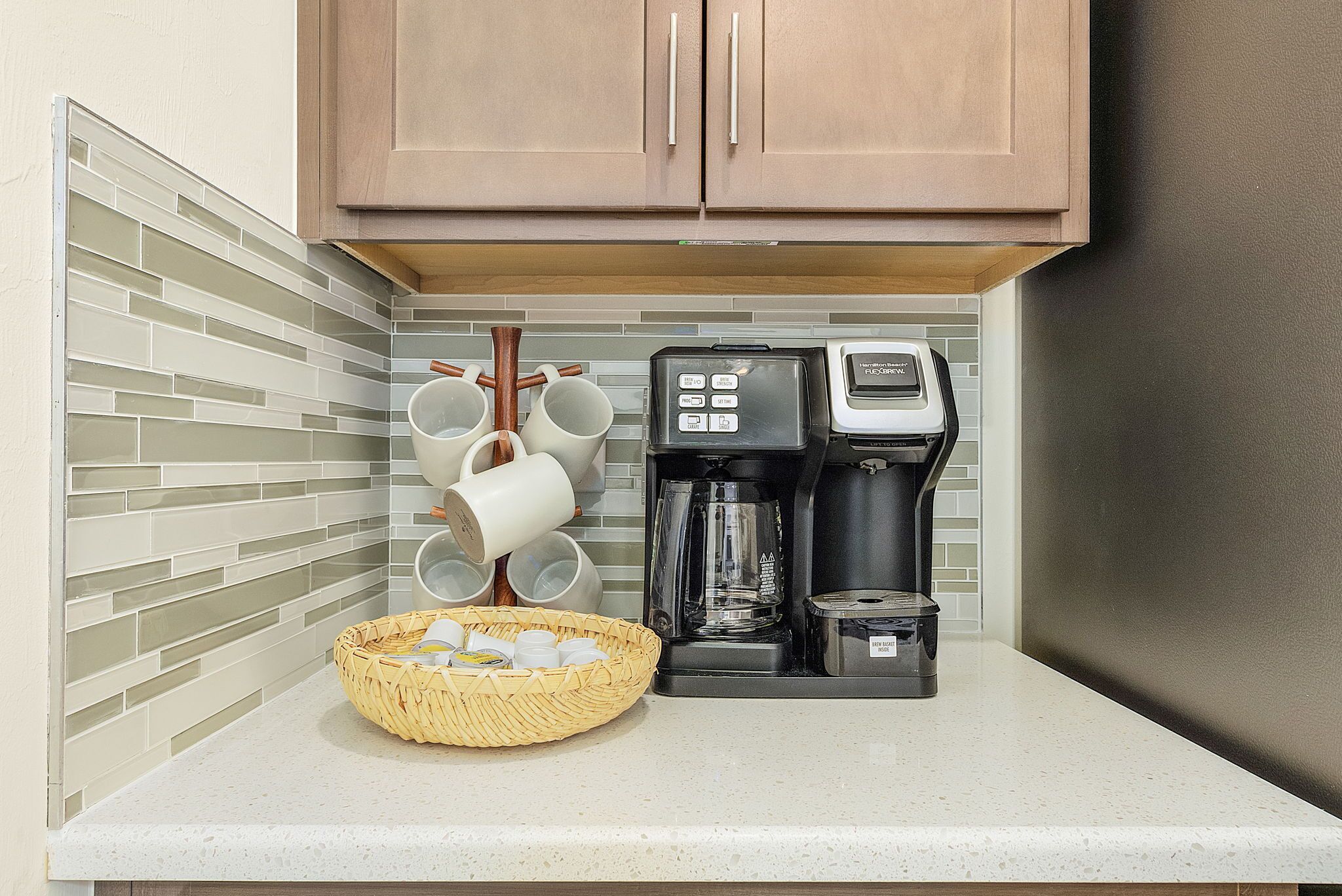 A kitchen with a coffee maker, a basket of cups, and a hanging mug rack.