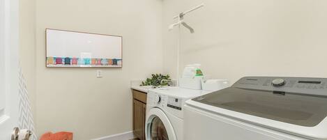A compact laundry room with a washing machine, dryer, and a wall-mounted shelf with folded clothes.