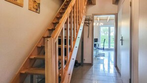 Un escalier en bois mène à une pièce dotée d’une porte en verre, d’un ordinateur portable posé sur une table et d’une chaise.