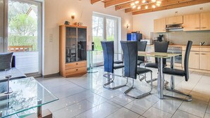 Une cuisine moderne avec des poutres en bois, un coin repas avec une table en verre et des chaises noires, et un grand meuble avec des portes en verre.