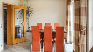 Un comedor con una mesa de madera y sillas anaranjadas, una planta en maceta y una puerta de madera con paneles de vidrio.