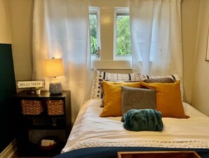 Cozy retreat with a bed, bedside table, and lamp, offering a peaceful view of the surrounding greenery.