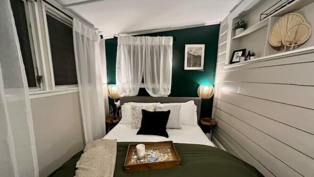 Ein schmales Hotelzimmer mit einem Bett, einem Nachttisch und einem Fenster mit Vorhängen.