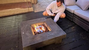 Eine Person sitzt auf einer Terrasse mit einem Feuerkorb vor sich.