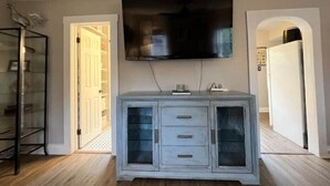 Ein Wohnzimmer mit einem flachbildfernseher an der Wand, einer hellblauen Kommode und einem Glastrennschrank.