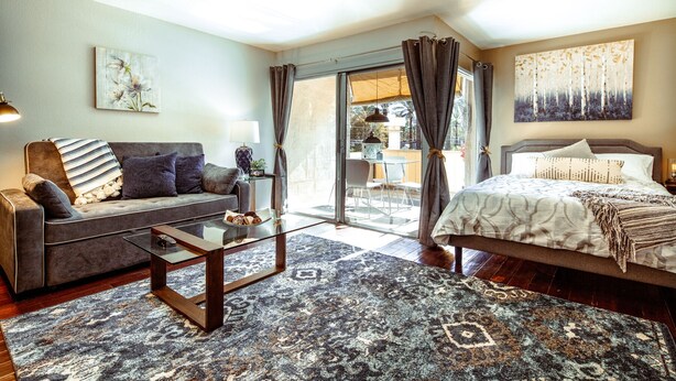 Een moderne slaapkamer met een bank, een bed, een bijzettafeltje en uitzicht op het groen.