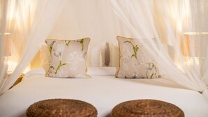Een bed met witte beddengoed, twee kussens met bloemenmotieven en een hemelbed.