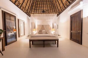 Ein Schlafzimmer mit einem Himmelsbett, einem Deckenventilator und einer großen Holztür.