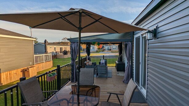 A covered outdoor deck with a table and chairs, a patio umbrella, and a view of neighboring houses. - Paradise in Niagara-on-the-lakes at Vine Ridge Resorts.  (Niagara-on-the-Lake)