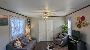 A living room with a grey sofa, a grey armchair, a coffee table, a ceiling fan, and a TV on a stand. - Paradise in Niagara-on-the-lakes at Vine Ridge Resorts.  (Niagara-on-the-Lake)