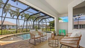 A covered outdoor area with a pool, wicker furniture, and a view of palm trees and houses. - Stunning villa with heated saltwater pool, 4 bedrooms, 2 bathrooms and office. (Cape Coral)