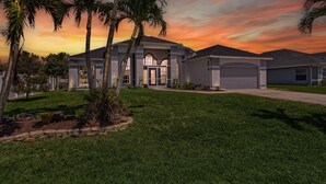 A modern two-story house with a well-maintained lawn, palm trees, and a garage. - Stunning villa with heated saltwater pool, 4 bedrooms, 2 bathrooms and office. (Cape Coral)
