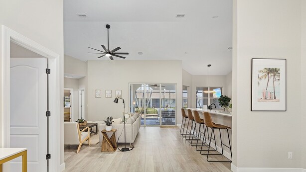 A spacious living area with a sofa, coffee table, and a dining area with bar stools. There is a ceiling fan and a large window providing natural light. - Stunning villa with heated saltwater pool, 4 bedrooms, 2 bathrooms and office. (Cape Coral)