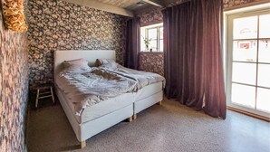 Una camera da letto con parete a effetto pietra, un letto con testiera bianca e una finestra con tende viola.