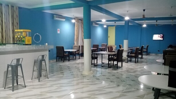 Un amplio comedor interior con paredes azules, varias mesas y sillas, una zona de bar con taburetes y ventiladores de techo.