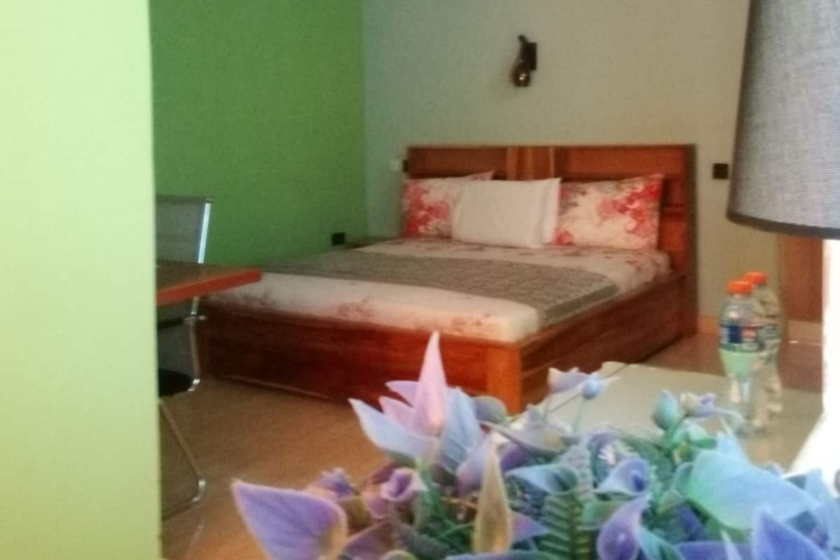 A bedroom with a bed, a nightstand, a lamp, and a plant.