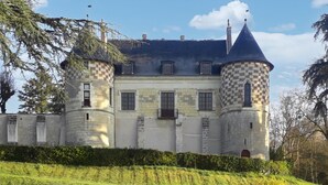 A castle-like building with two towers, a central entrance, and a surrounding hedge.
