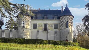 Un bâtiment qui ressemble à un château, avec deux tours, une entrée centrale et une haie qui l’entoure.