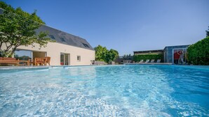 A clear swimming pool with lounge chairs and a building with a sloped roof.