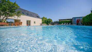 Une piscine aux eaux cristallines, dotée de chaises longues, et un bâtiment avec un toit en pente.