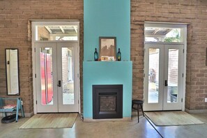 A room with a fireplace, a door, and a view through the glass doors. - Barrio Viejo, Charming Historic Downtown Home (Tucson)