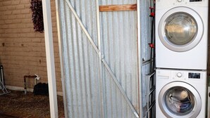 Une buanderie équipée d’un lave-linge et d’un sèche-linge, avec une porte en métal et un mur en briques.