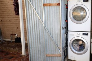 A laundry area with a washing machine and dryer, a metal door, and a brick wall. - Barrio Viejo, Charming Historic Downtown Home (Tucson)